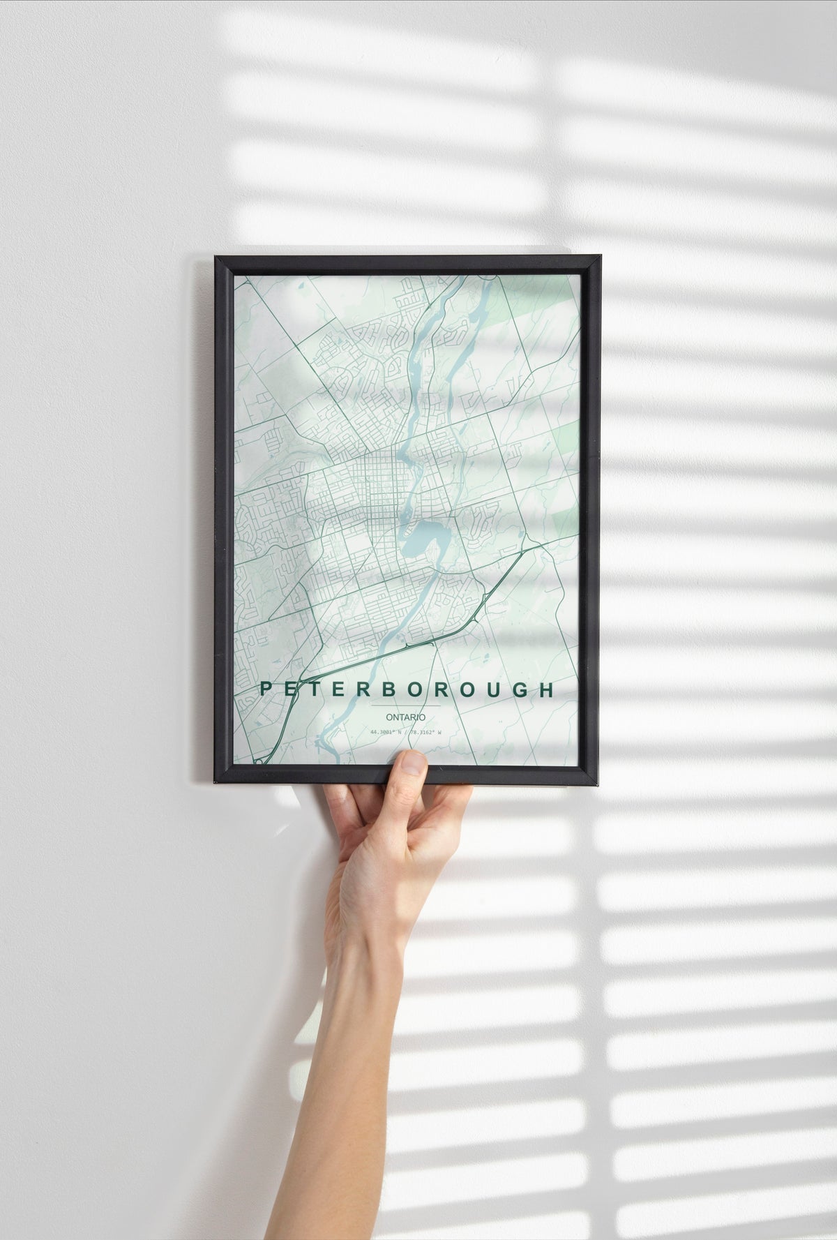 Peterborough, Ontario, Canada map print in the Forest theme in a black frame held against a pale wall