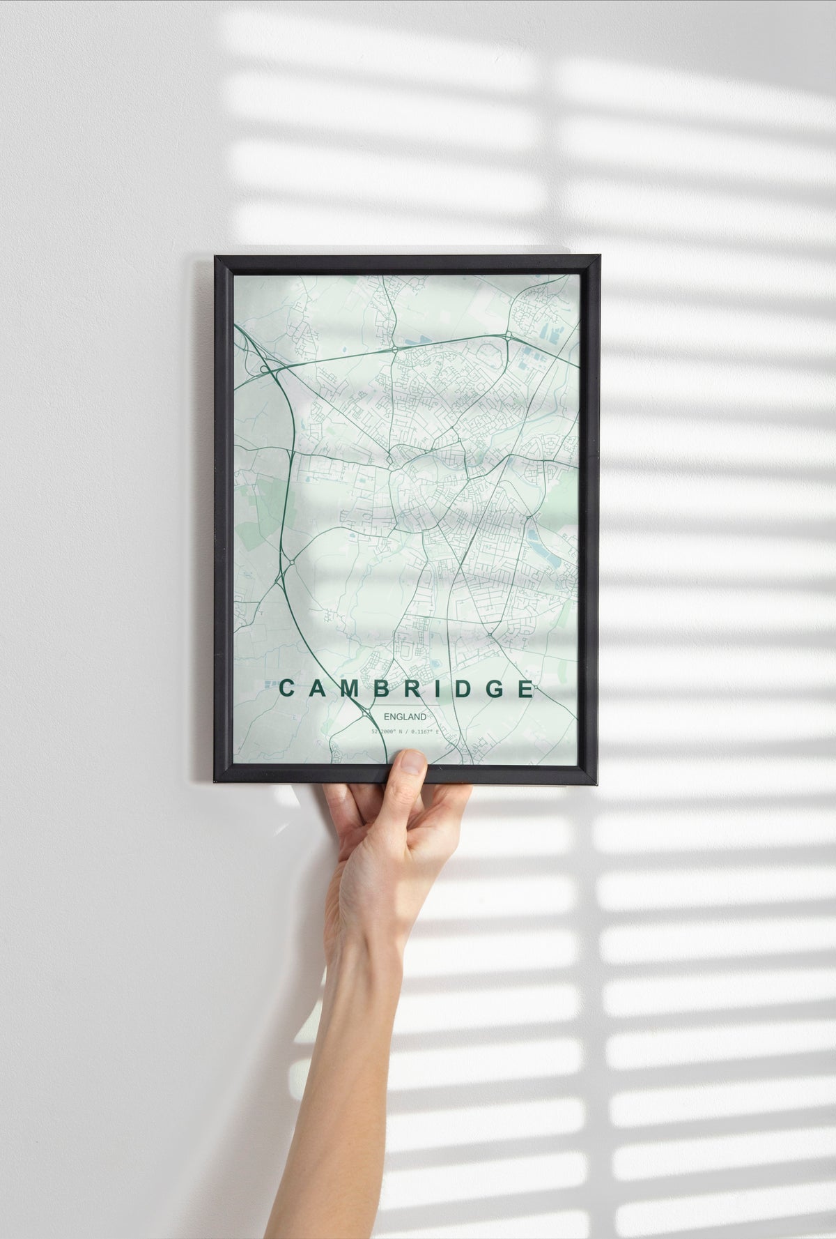 Cambridge map print in the Forest theme in a black frame held against a pale wall