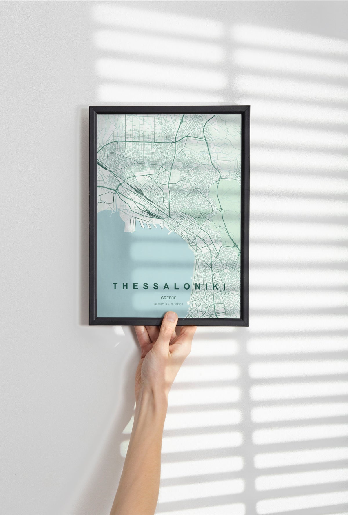 Thessaloniki map print in the Forest theme in a black frame held against a pale wall