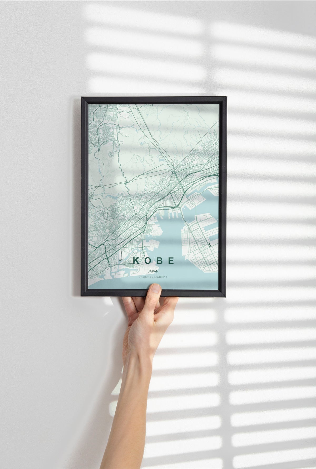 Kobe, Japan map print in the Forest theme in a black frame held against a pale wall