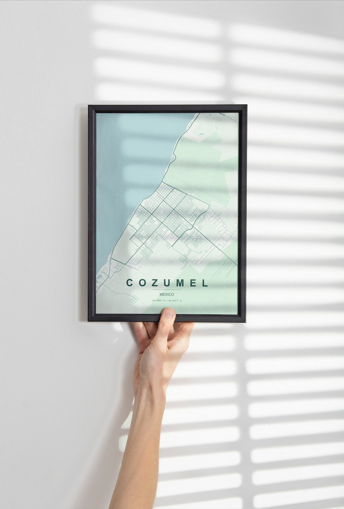 Cozumel, Mexico map print in the Forest theme in a black frame held against a pale wall