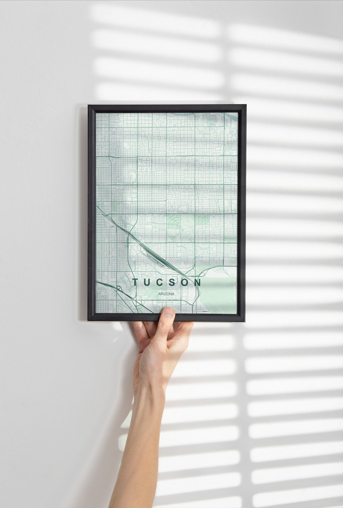 Tucson map print in the Forest theme in a black frame held against a pale wall