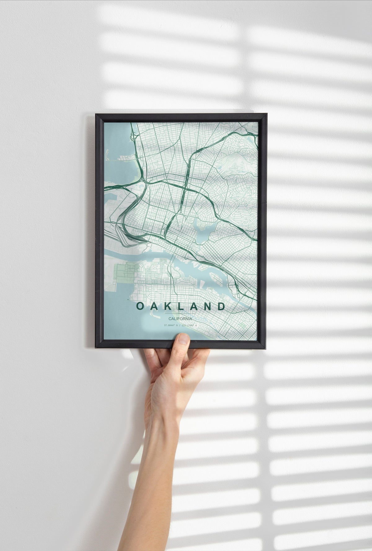 Oakland map print in the Forest theme in a black frame held against a pale wall