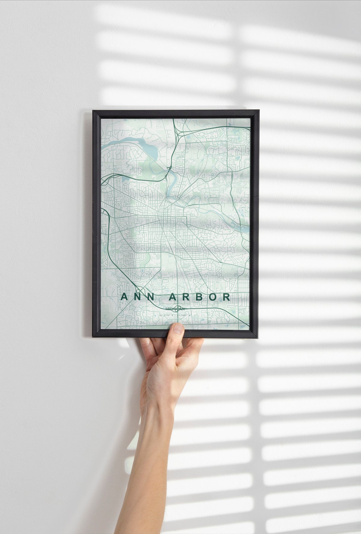 Ann Arbor map print in the Forest theme in a black frame held against a pale wall