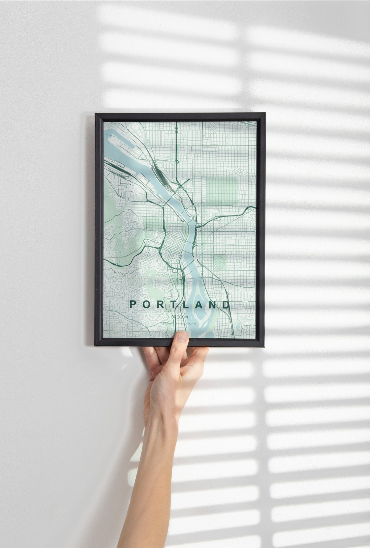 Portland, Oregon map print in the Forest theme in a black frame held against a pale wall