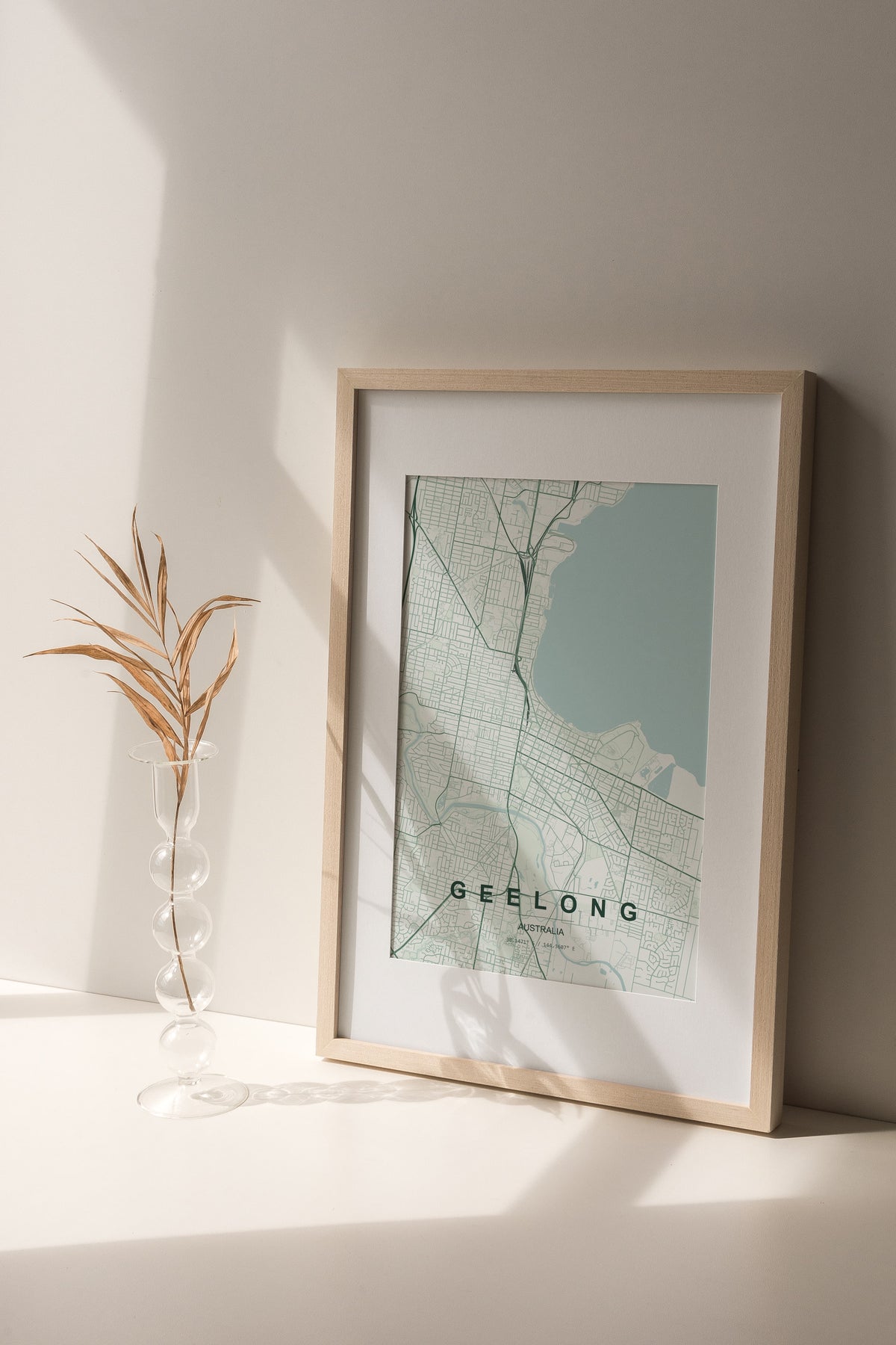 Geelong, Victoria, Australia map print in the Forest theme in a light wooden frame on a shelf beside a glass vase