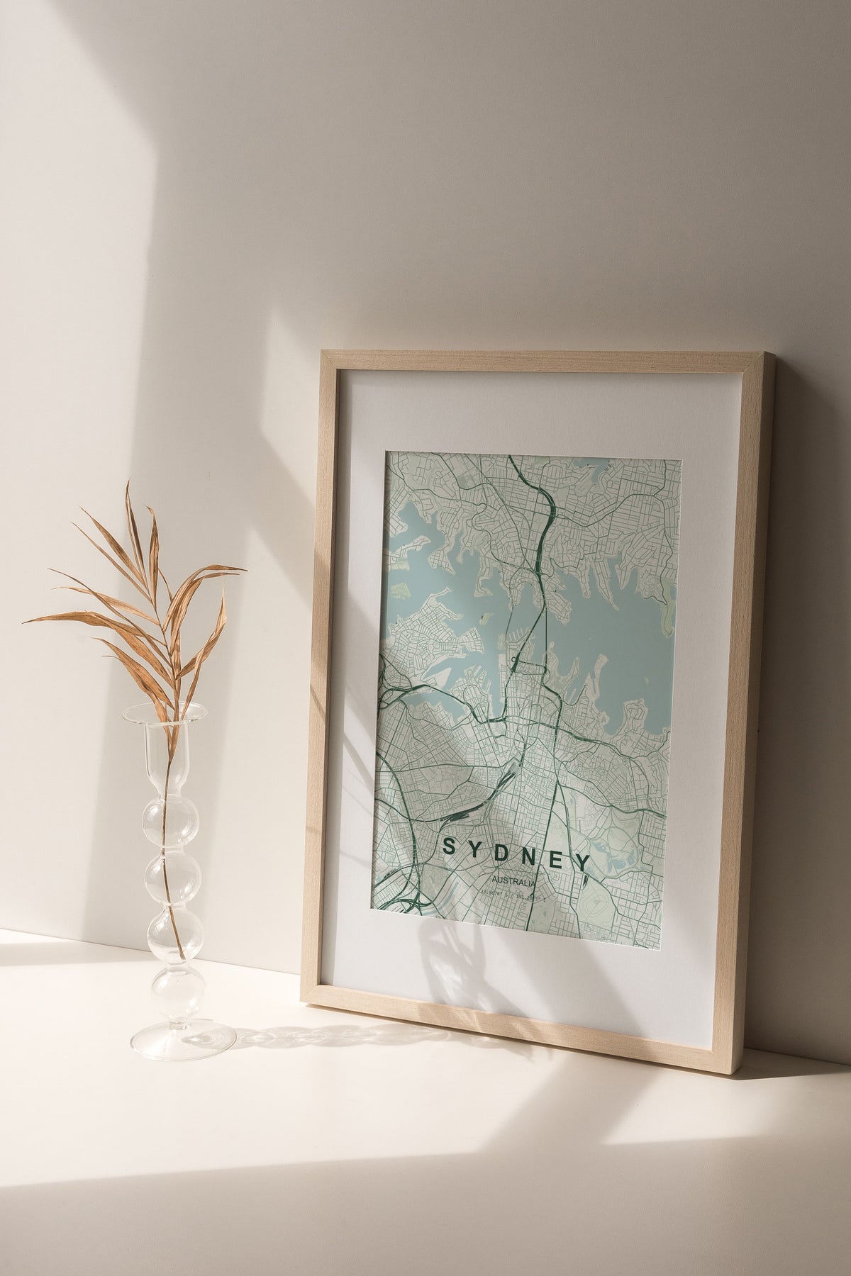 Sydney, New South Wales, Australia map print in the Forest theme in a light wooden frame on a shelf beside a glass vase