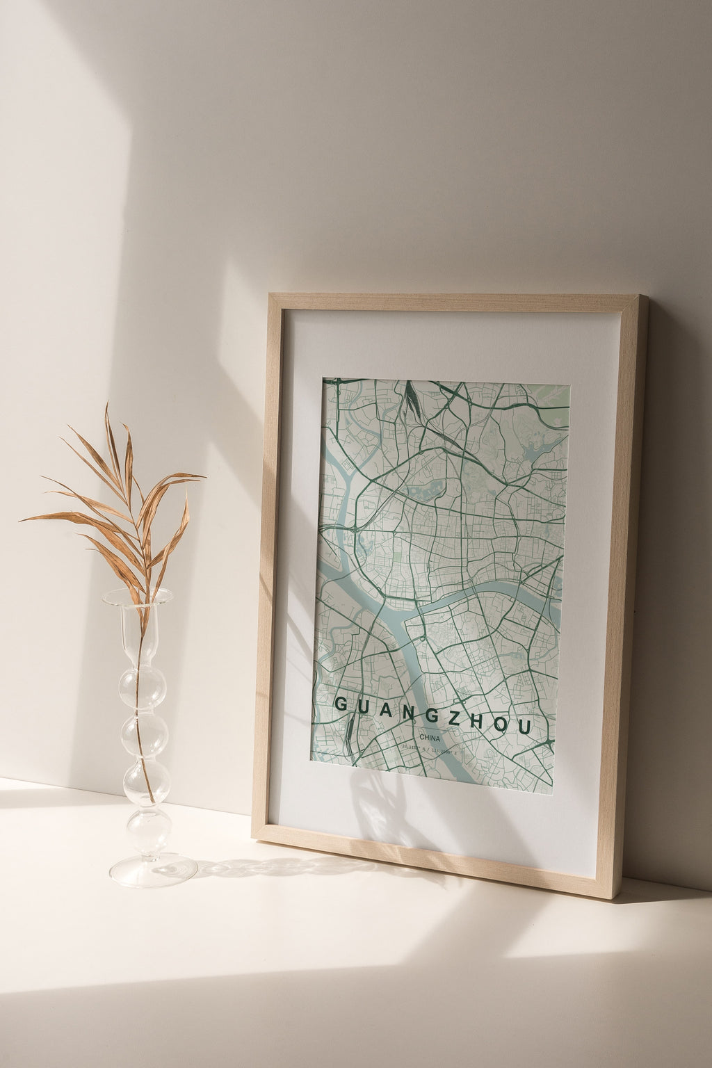 Guangzhou, China map print in the Forest theme in a light wooden frame on a shelf beside a glass vase
