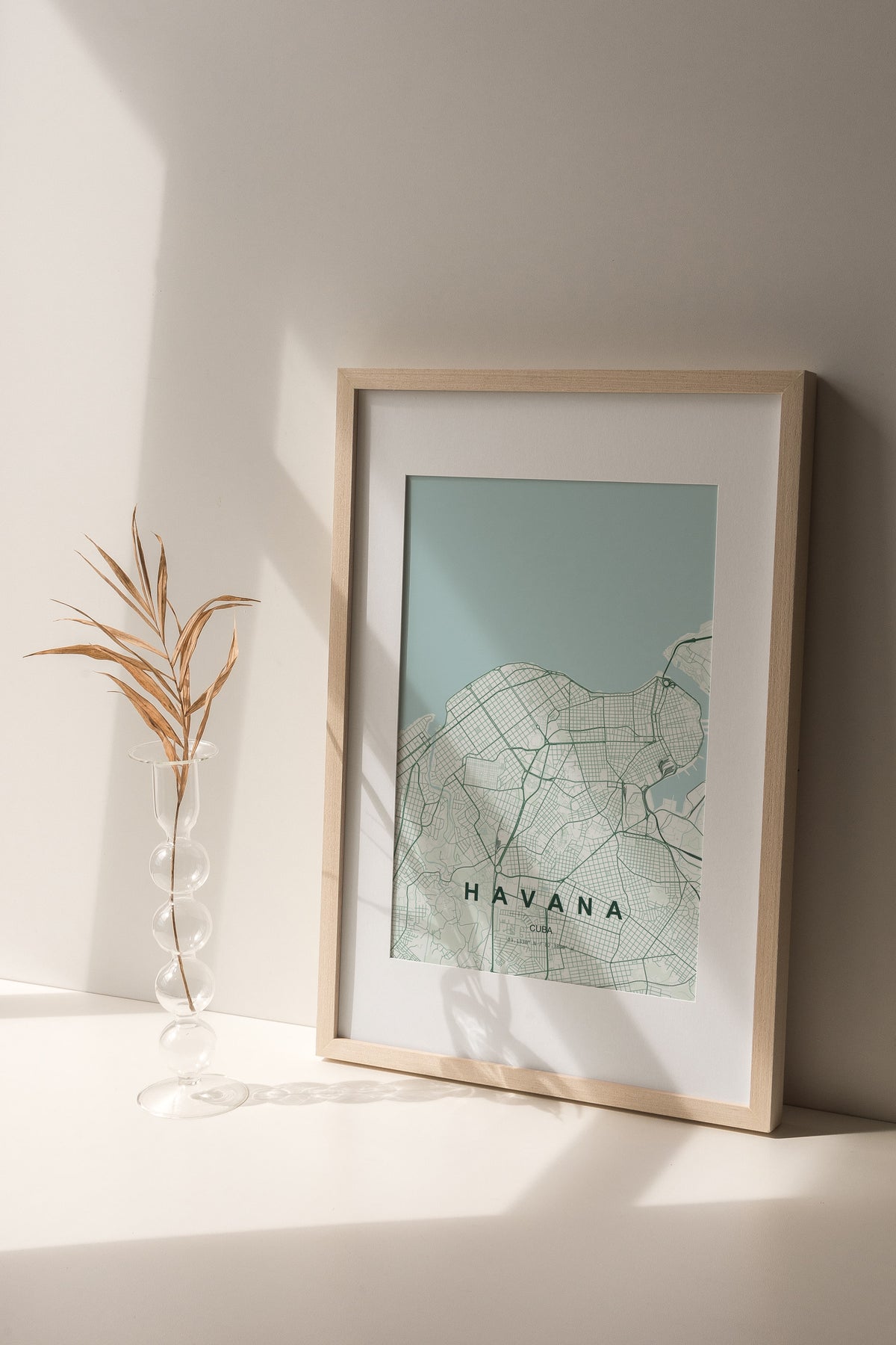 Havana, Cuba map print in the Forest theme in a light wooden frame on a shelf beside a glass vase