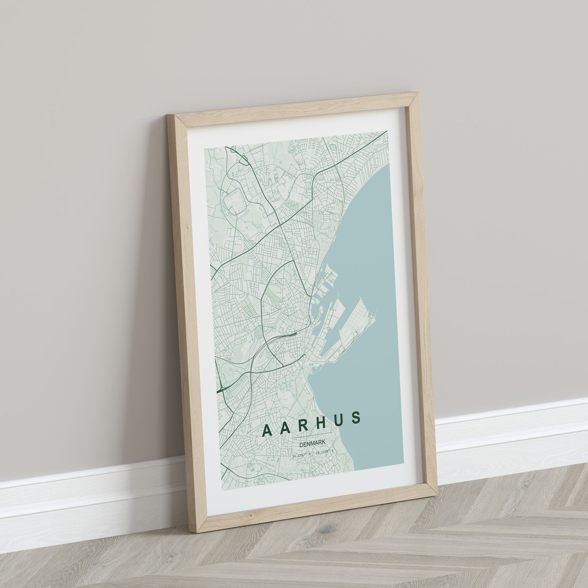 Aarhus map print in the Forest theme in a light wooden frame leaning against a pale wall
