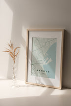Aarhus map print in the Forest theme in a light wooden frame on a shelf beside a glass vase