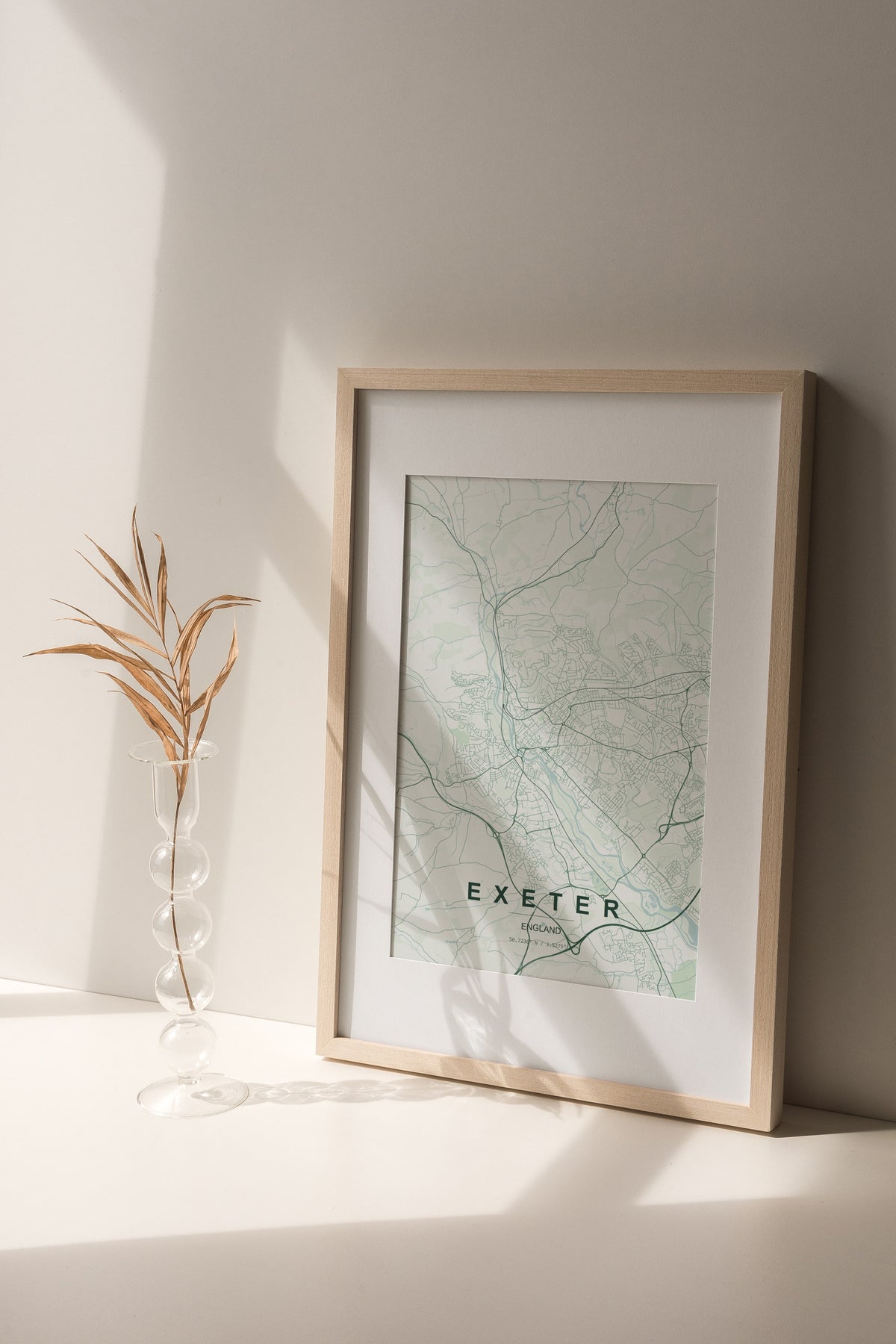 Exeter, England, United Kingdom map print in the Forest theme in a light wooden frame on a shelf beside a glass vase