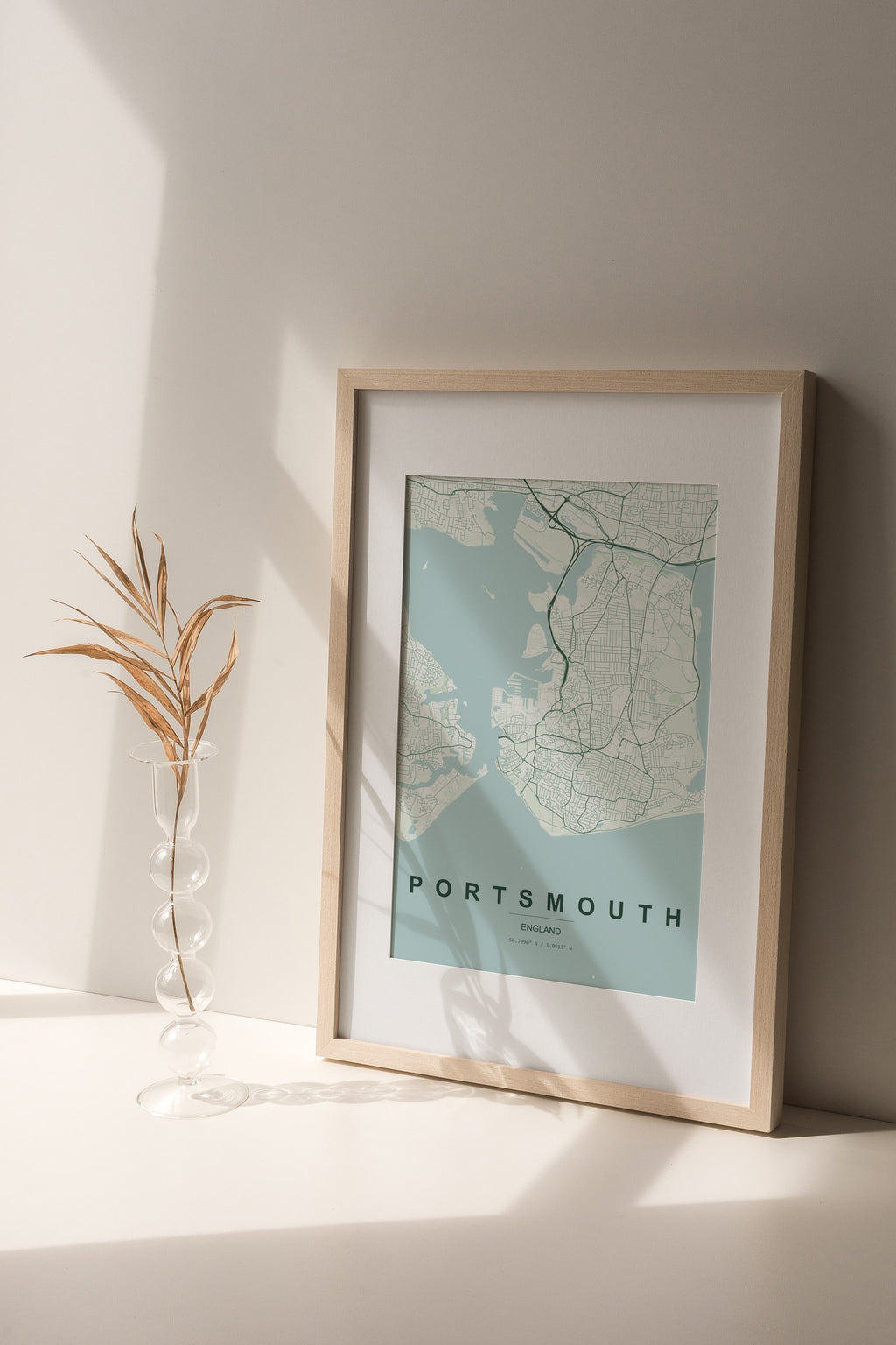 Portsmouth, England, United Kingdom map print in the Forest theme in a light wooden frame on a shelf beside a glass vase