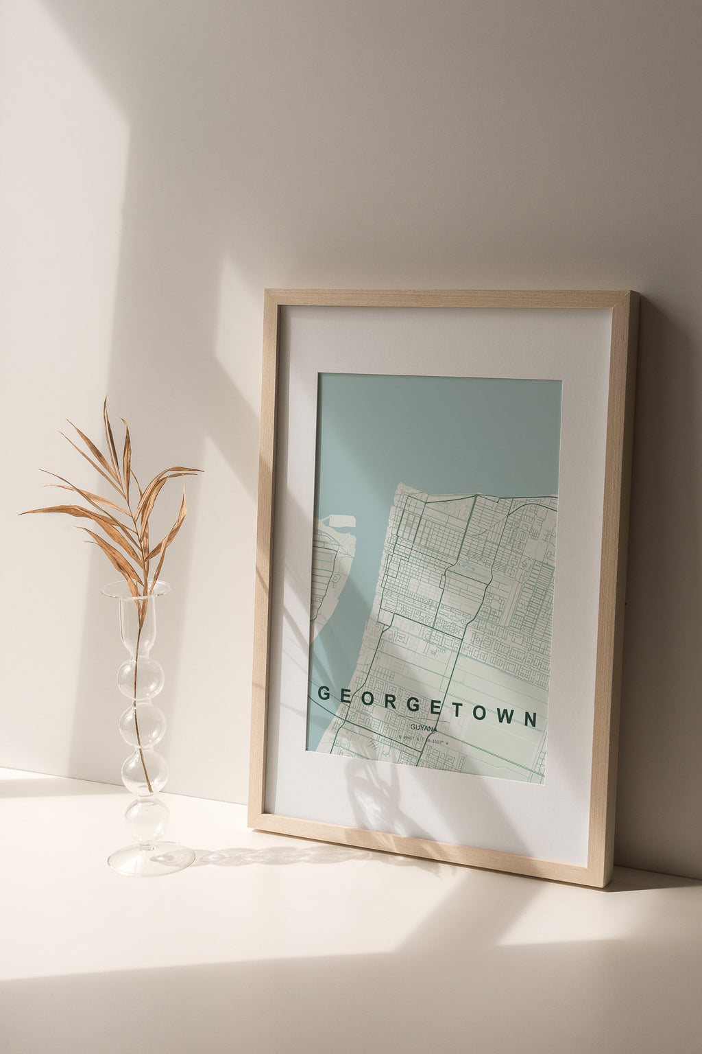 Georgetown, Guyana map print in the Forest theme in a light wooden frame on a shelf beside a glass vase