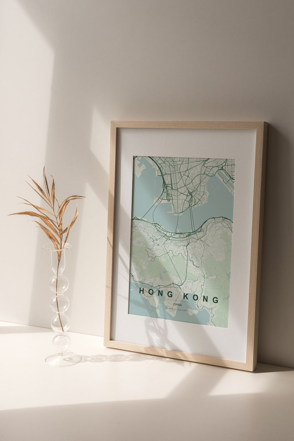 Hong Kong, China map print in the Forest theme in a light wooden frame on a shelf beside a glass vase