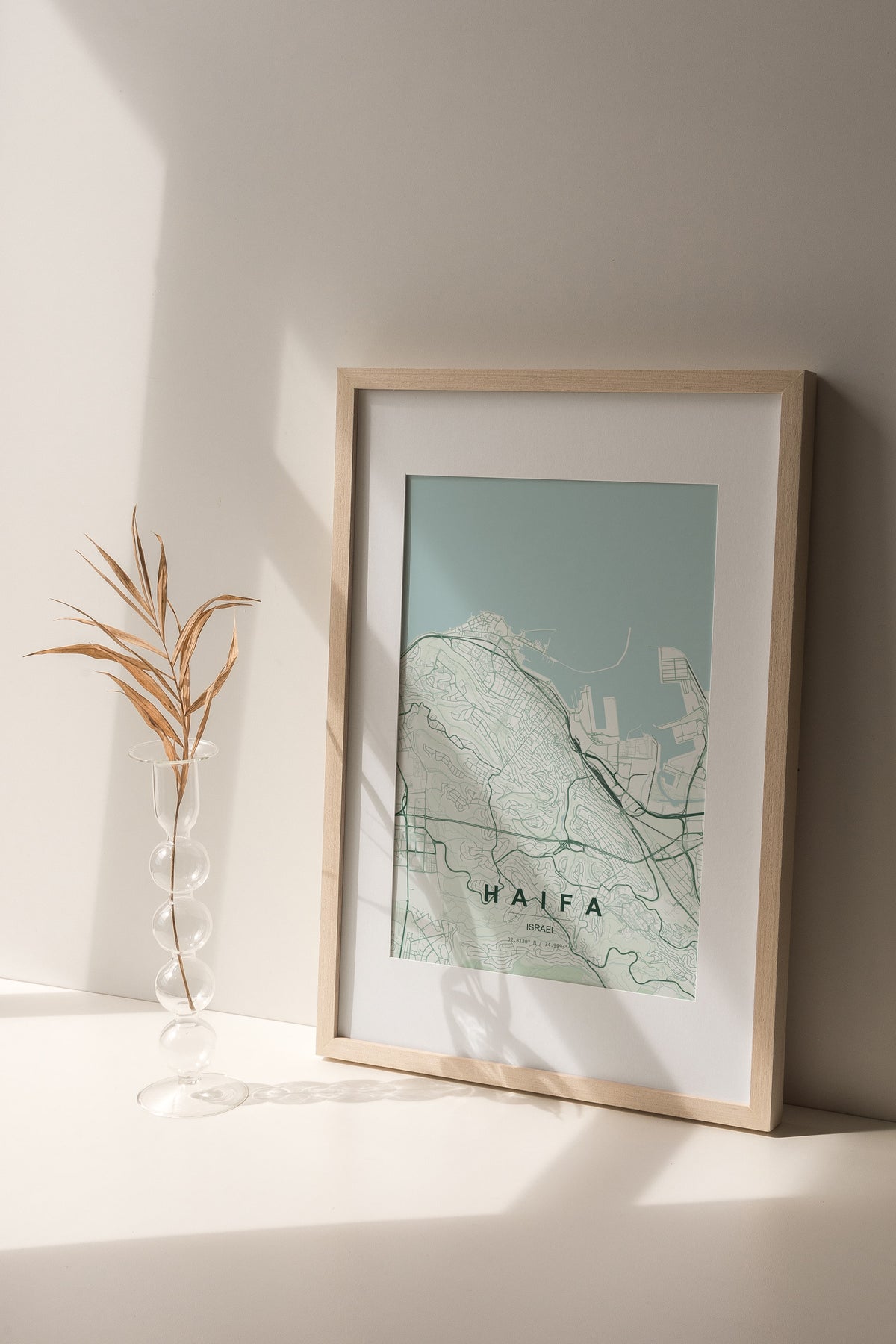 Haifa, Israel map print in the Forest theme in a light wooden frame on a shelf beside a glass vase