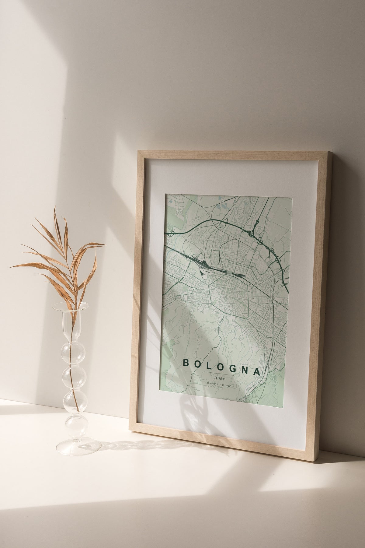 Bologna map print in the Forest theme in a light wooden frame on a shelf beside a glass vase