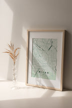 Milan map print in the Forest theme in a light wooden frame on a shelf beside a glass vase