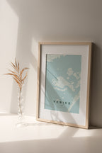 Venice map print in the Forest theme in a light wooden frame on a shelf beside a glass vase