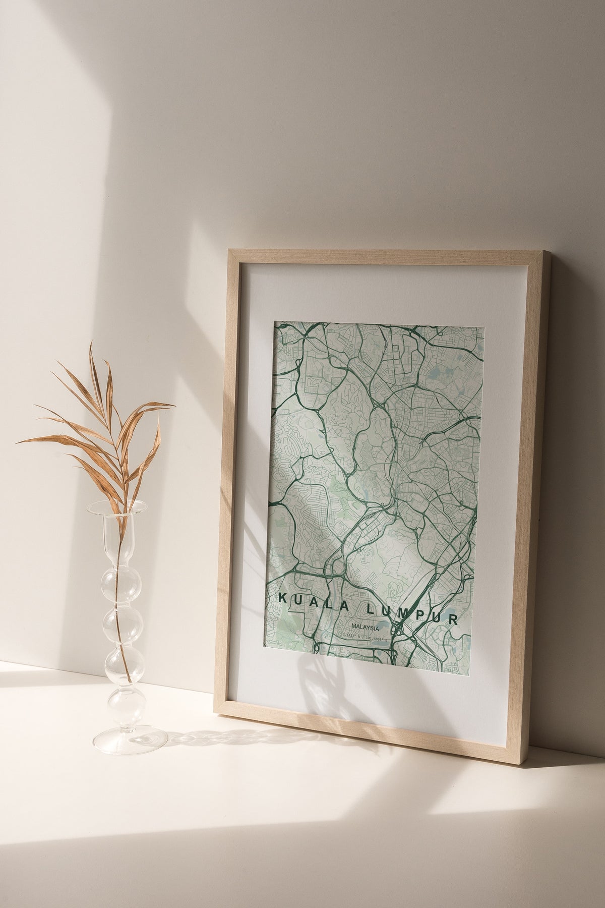 Kuala Lumpur, Malaysia map print in the Forest theme in a light wooden frame on a shelf beside a glass vase