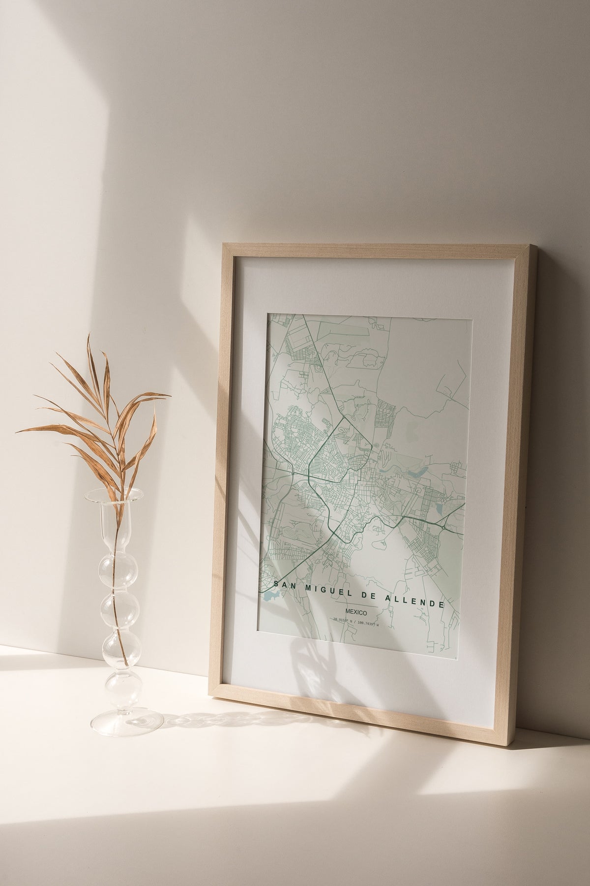 San Miguel de Allende, Mexico map print in the Forest theme in a light wooden frame on a shelf beside a glass vase