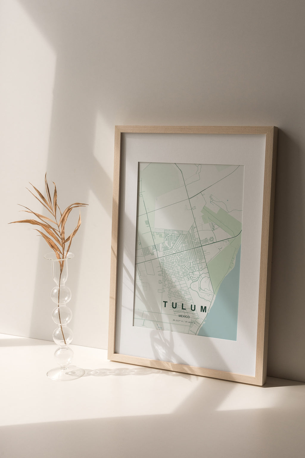 Tulum, Mexico map print in the Forest theme in a light wooden frame on a shelf beside a glass vase