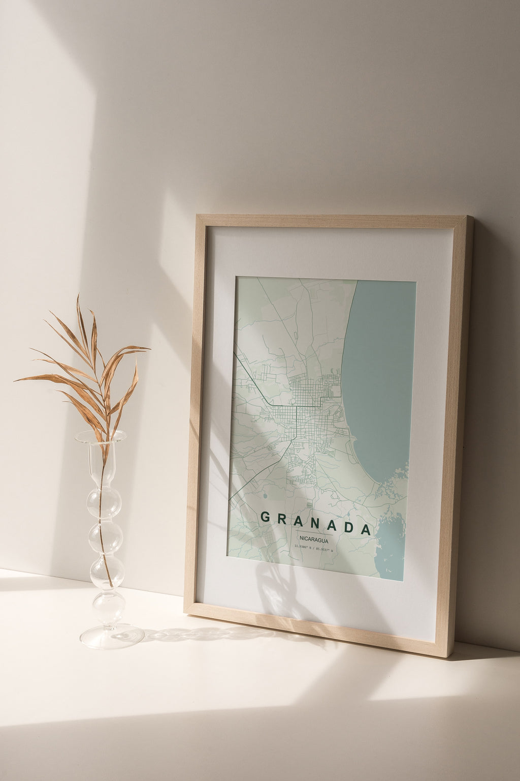 Granada, Nicaragua map print in the Forest theme in a light wooden frame on a shelf beside a glass vase