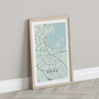Doha, Qatar map print in the Forest theme in a light wooden frame leaning against a pale wall