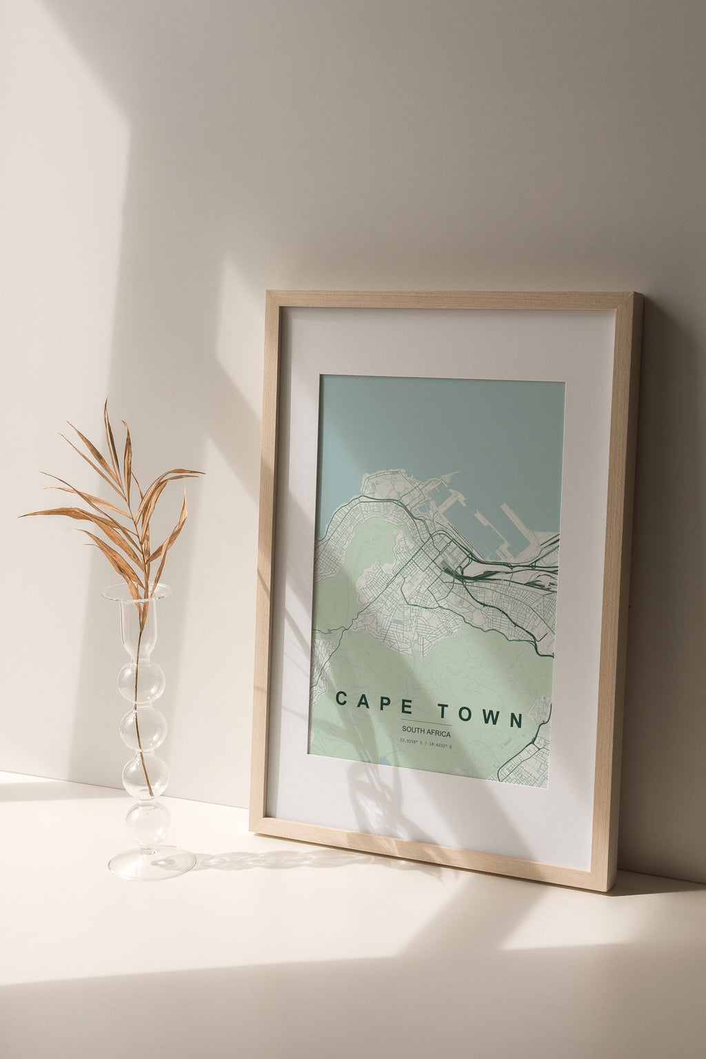 Cape Town, Western Cape, South Africa map print in the Forest theme in a light wooden frame on a shelf beside a glass vase