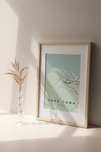 Cape Town, Western Cape, South Africa map print in the Forest theme in a light wooden frame on a shelf beside a glass vase
