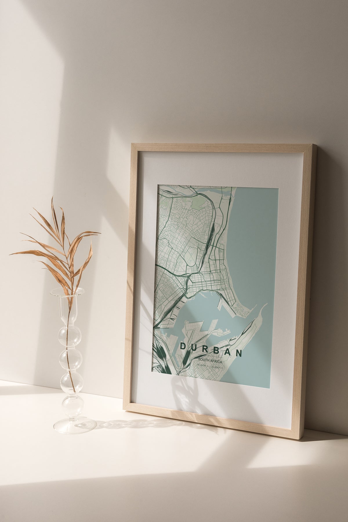 Durban, KwaZulu-Natal, South Africa map print in the Forest theme in a light wooden frame on a shelf beside a glass vase