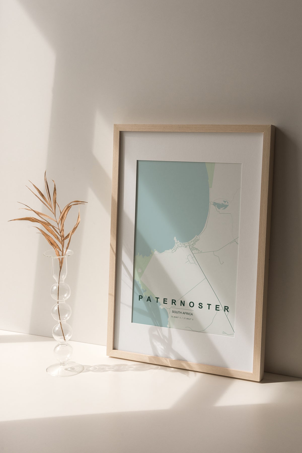 Paternoster, Western Cape, South Africa map print in the Forest theme in a light wooden frame on a shelf beside a glass vase