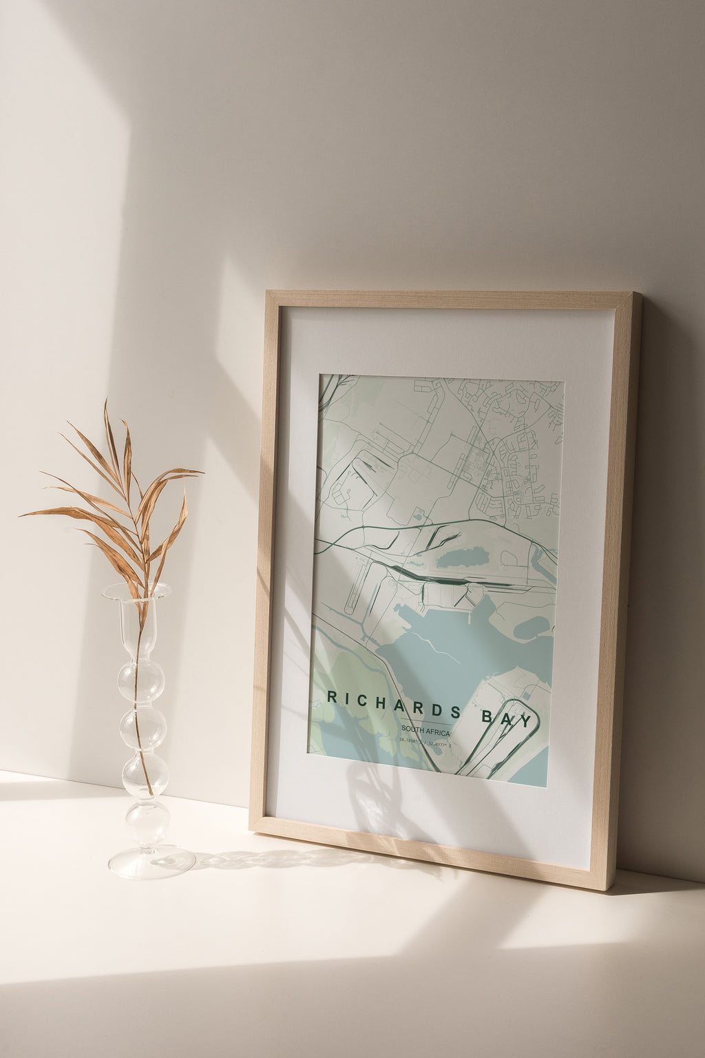 Richards Bay, KwaZulu-Natal, South Africa map print in the Forest theme in a light wooden frame on a shelf beside a glass vase