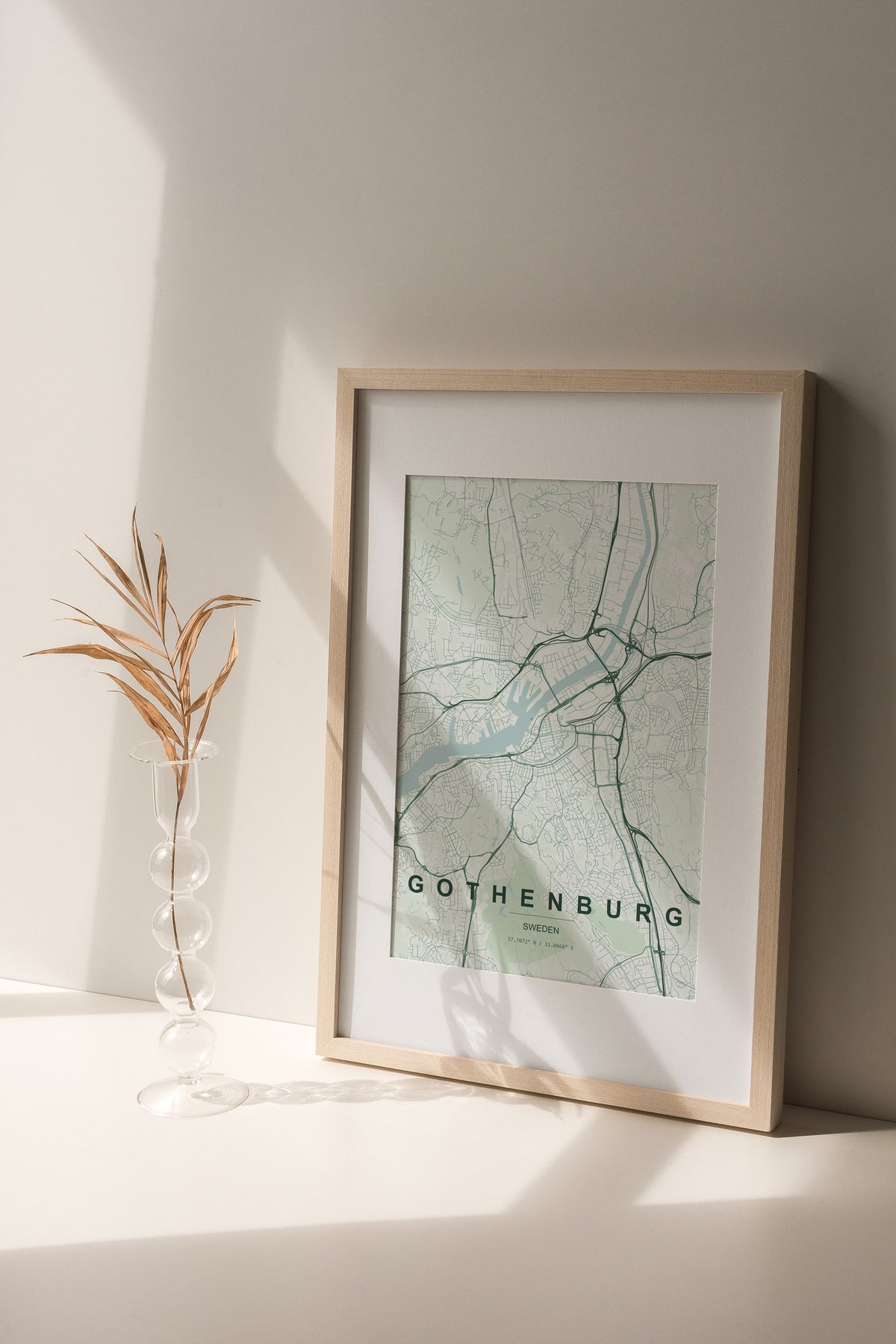 Gothenburg map print in the Forest theme in a light wooden frame on a shelf beside a glass vase