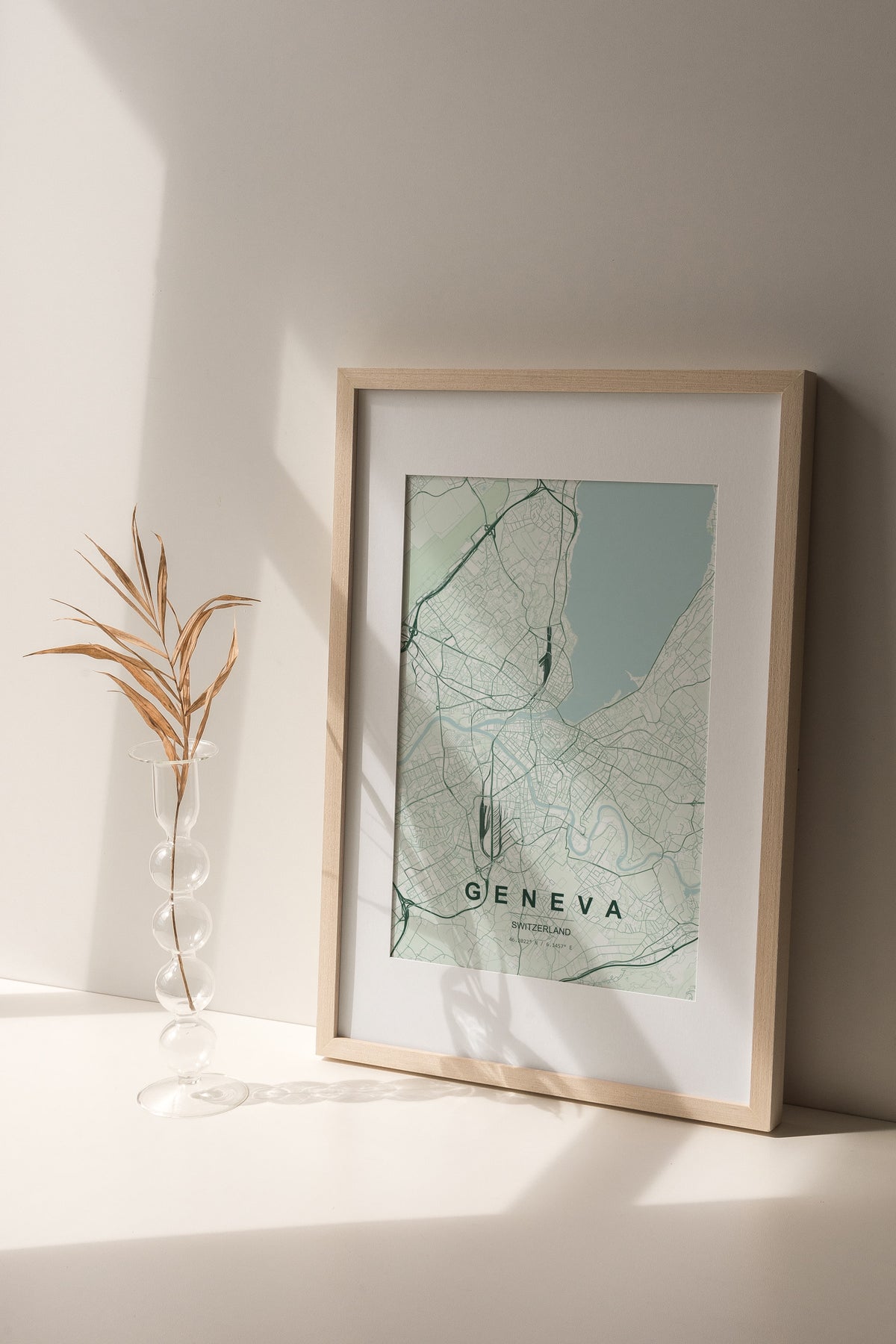 Geneva map print in the Forest theme in a light wooden frame on a shelf beside a glass vase