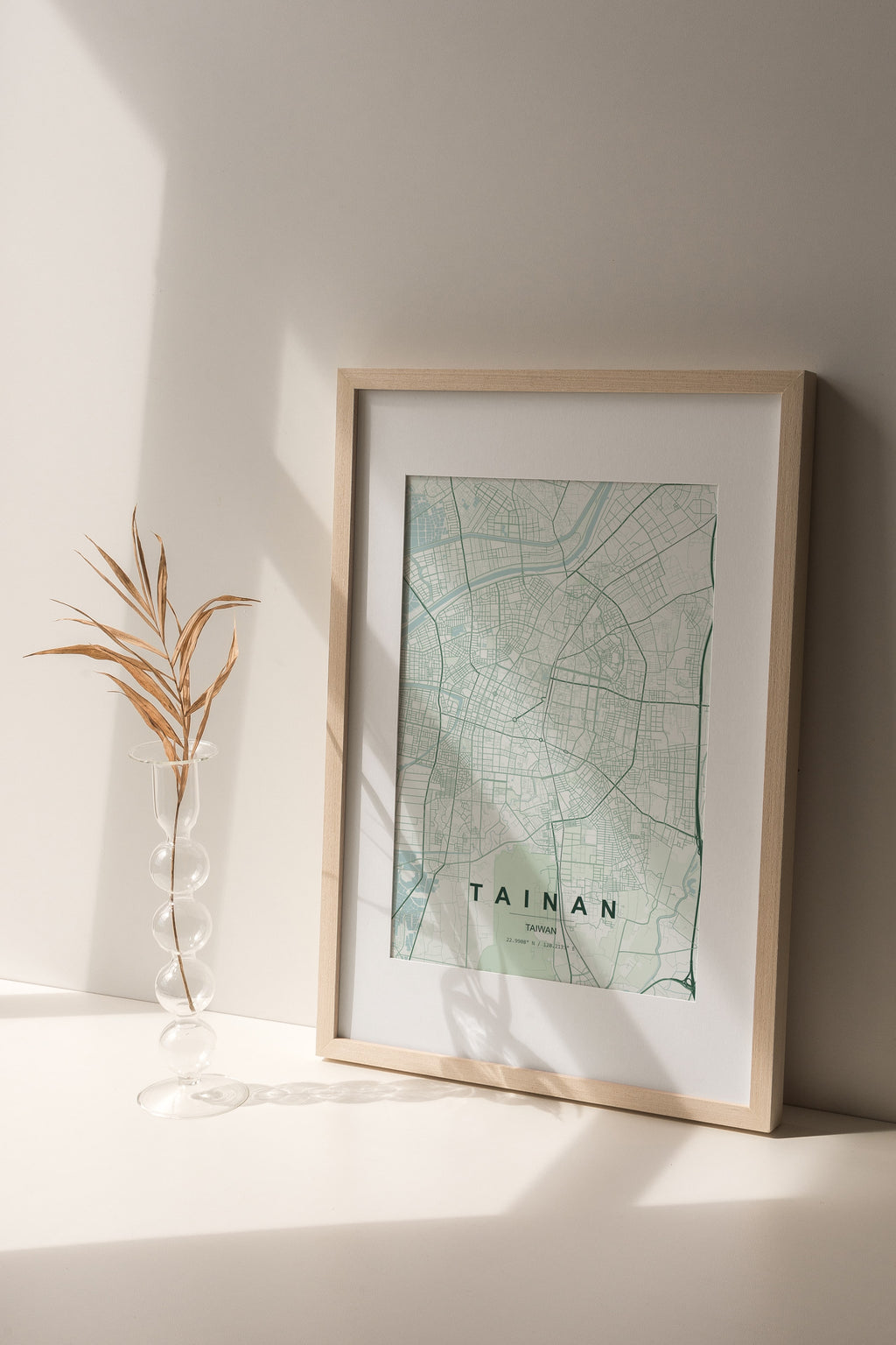 Tainan, Taiwan map print in the Forest theme in a light wooden frame on a shelf beside a glass vase