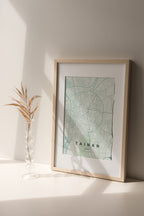 Tainan, Taiwan map print in the Forest theme in a light wooden frame on a shelf beside a glass vase