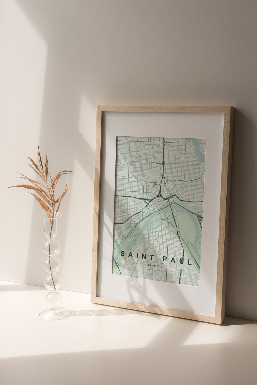Saint Paul map print in the Forest theme in a light wooden frame on a shelf beside a glass vase