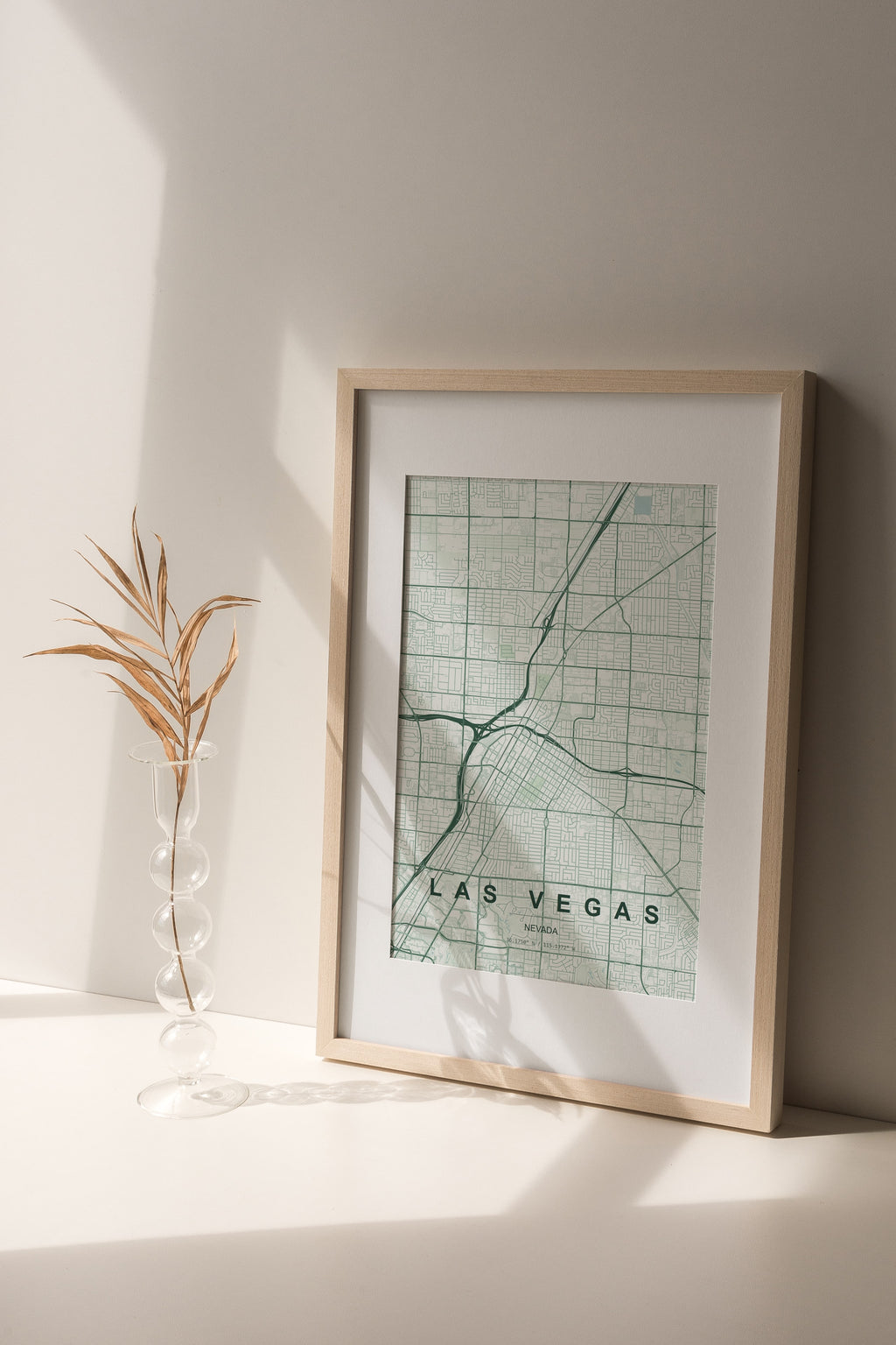 Las Vegas map print in the Forest theme in a light wooden frame on a shelf beside a glass vase