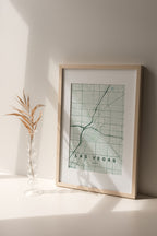 Las Vegas map print in the Forest theme in a light wooden frame on a shelf beside a glass vase