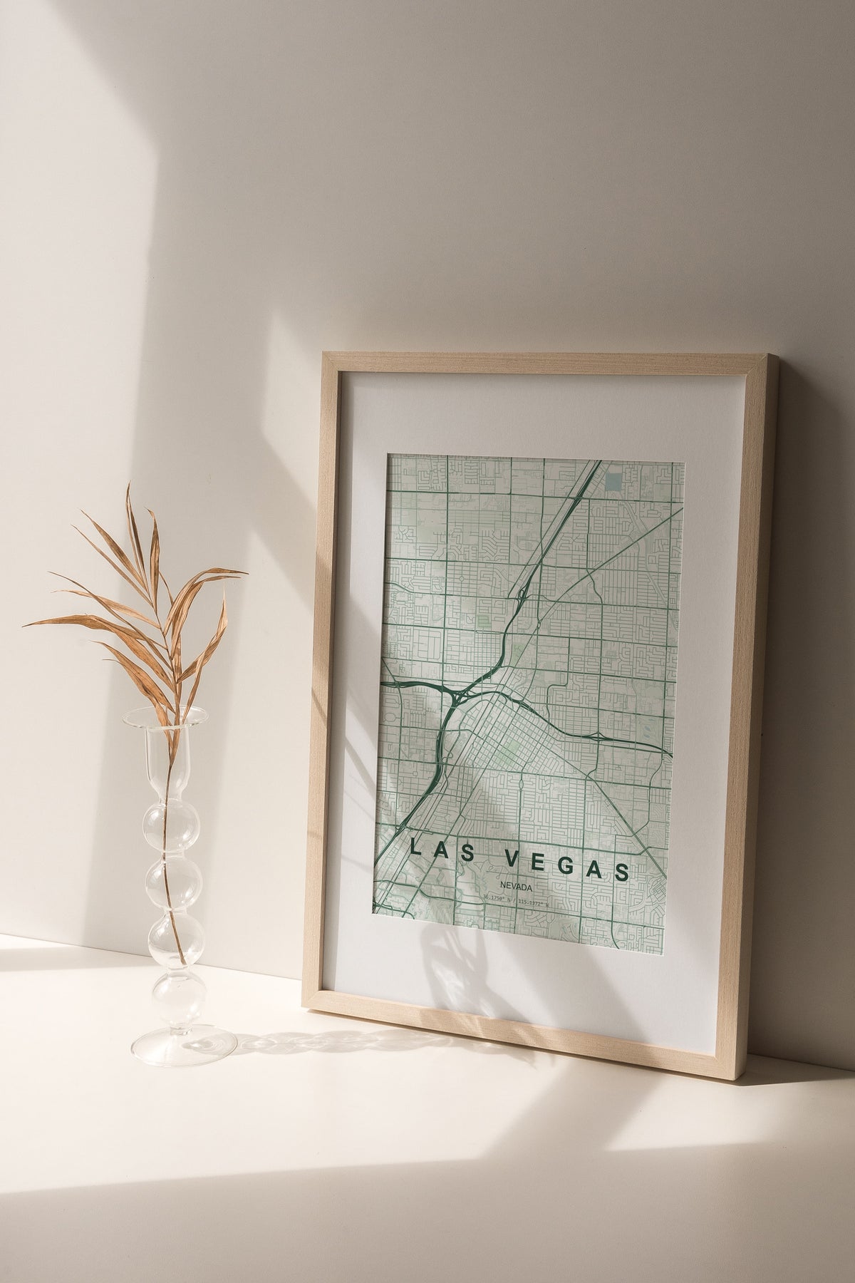 Las Vegas map print in the Forest theme in a light wooden frame on a shelf beside a glass vase