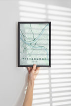 Pittsburgh map print in the Forest theme in a black frame held against a pale wall