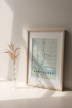 Vancouver map print in the Forest theme in a light wooden frame on a shelf beside a glass vase