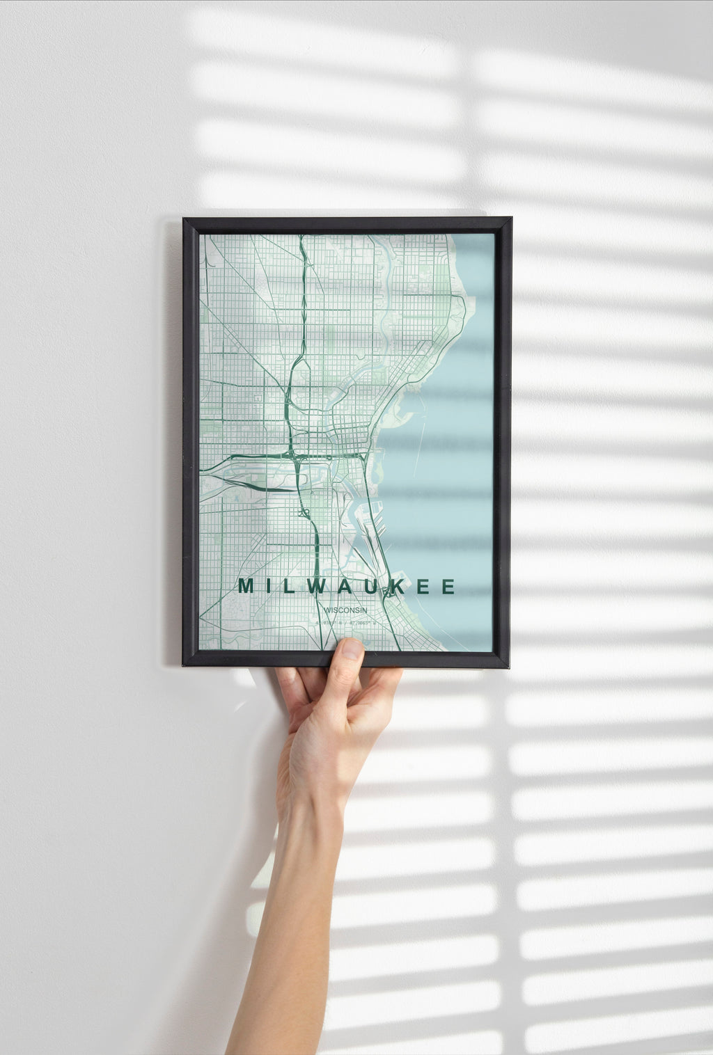 Milwaukee map print in the Forest theme in a black frame held against a pale wall