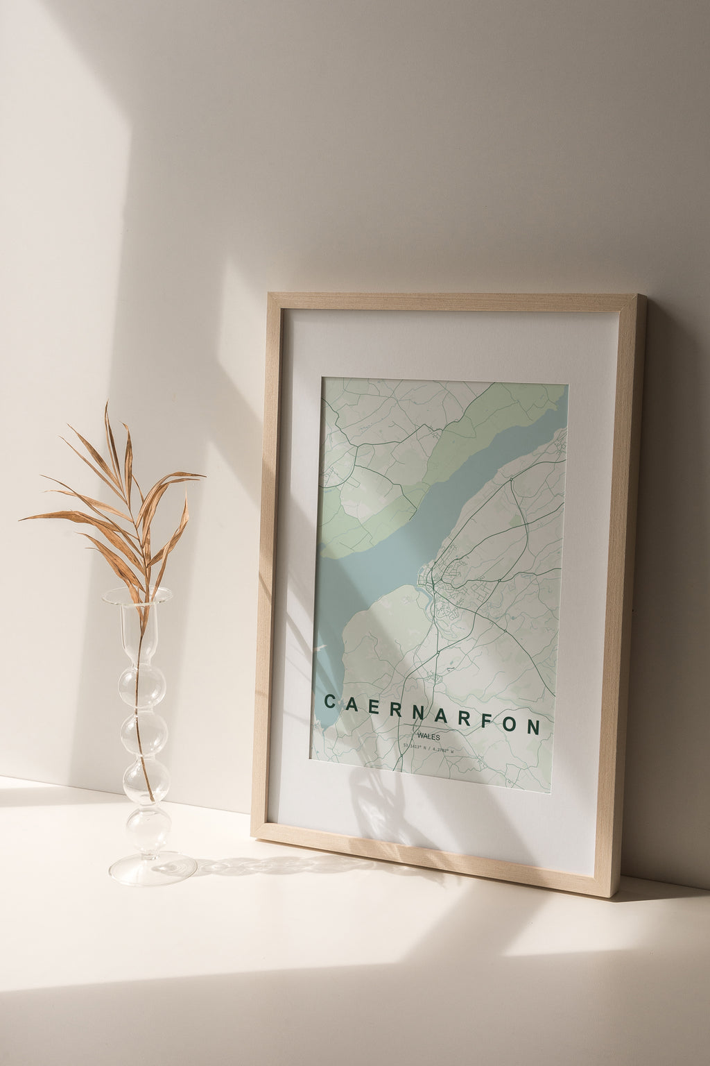 Caernarfon, Wales, United Kingdom map print in the Forest theme in a light wooden frame on a shelf beside a glass vase