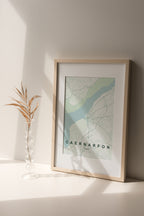 Caernarfon, Wales, United Kingdom map print in the Forest theme in a light wooden frame on a shelf beside a glass vase